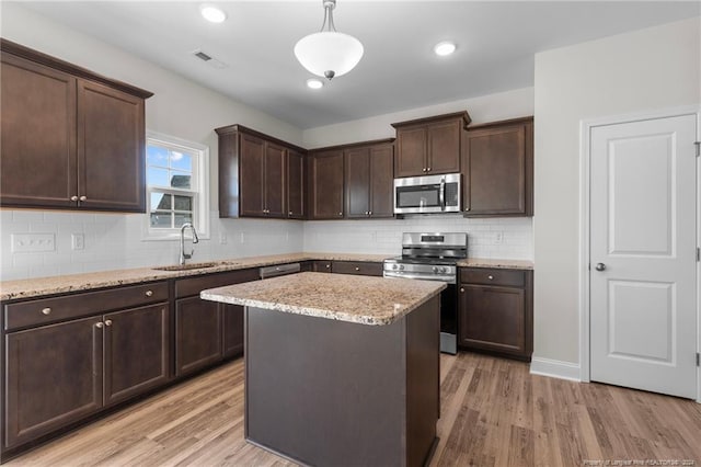 kitchen with sink, hanging light fixtures, light wood-type flooring, a kitchen island, and stainless steel appliances