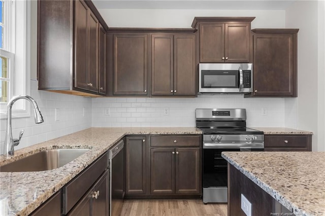 kitchen featuring light stone countertops, light wood-type flooring, dark brown cabinetry, stainless steel appliances, and sink