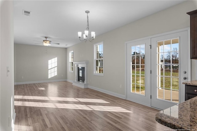 unfurnished living room featuring ceiling fan with notable chandelier, light hardwood / wood-style flooring, and a healthy amount of sunlight