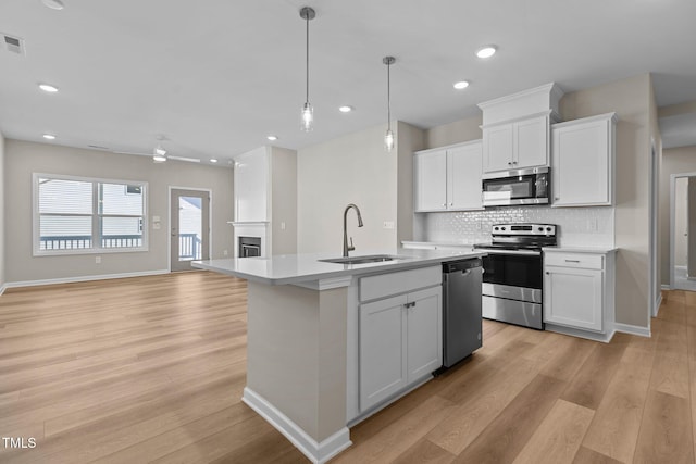 kitchen featuring white cabinets, appliances with stainless steel finishes, an island with sink, sink, and hanging light fixtures