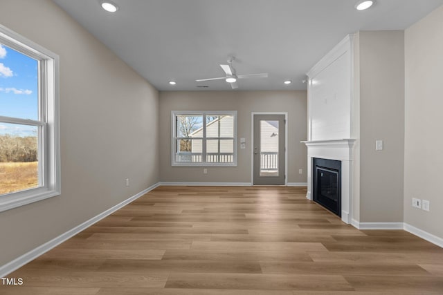 unfurnished living room with light hardwood / wood-style floors, a wealth of natural light, ceiling fan, and a fireplace