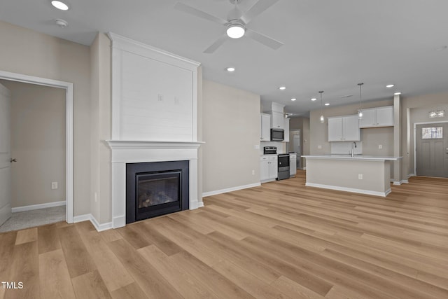 unfurnished living room with ceiling fan, a fireplace, sink, and light hardwood / wood-style flooring