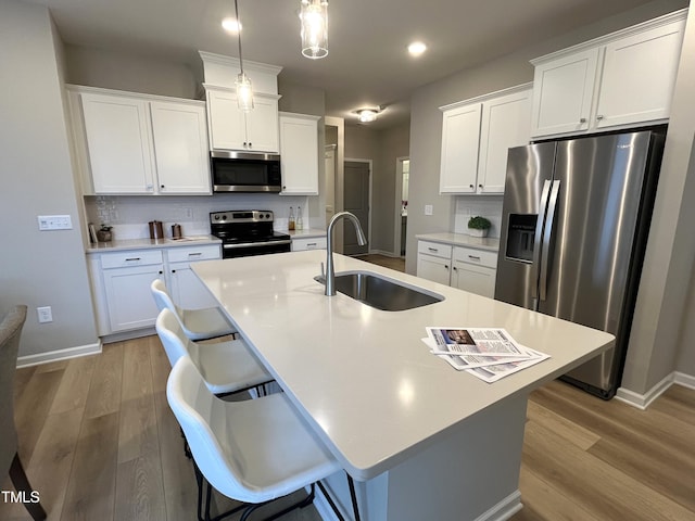 kitchen featuring sink, appliances with stainless steel finishes, a kitchen island with sink, hanging light fixtures, and a kitchen bar