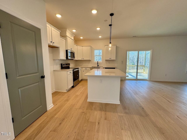 kitchen with pendant lighting, white cabinets, sink, appliances with stainless steel finishes, and a kitchen island