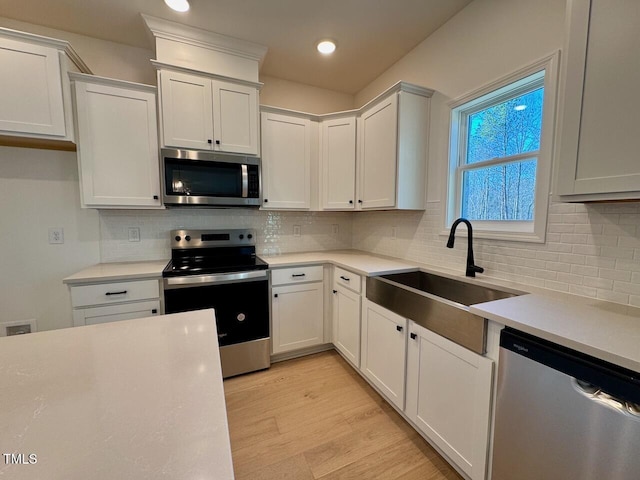 kitchen featuring sink, light hardwood / wood-style flooring, tasteful backsplash, white cabinetry, and stainless steel appliances