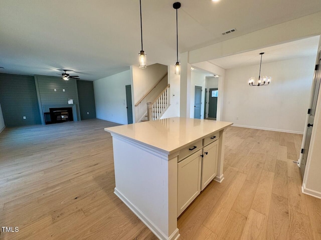 kitchen featuring white cabinetry, a center island, hanging light fixtures, light hardwood / wood-style flooring, and a fireplace