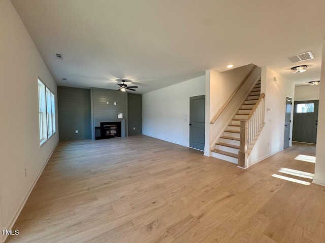 unfurnished living room featuring ceiling fan, a large fireplace, and light wood-type flooring