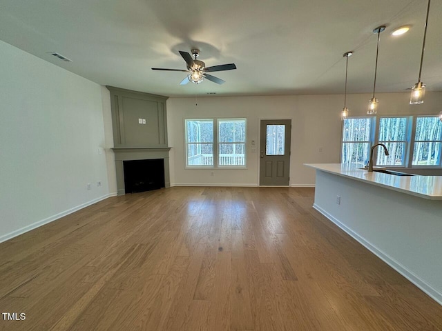 unfurnished living room with hardwood / wood-style flooring, sink, a large fireplace, and ceiling fan