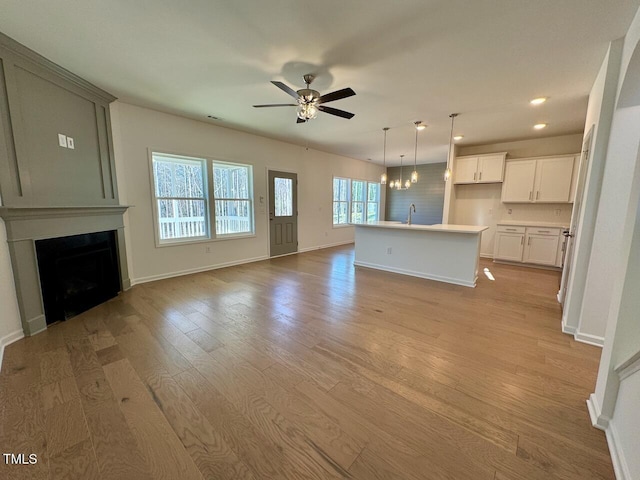 unfurnished living room with sink, ceiling fan with notable chandelier, and light hardwood / wood-style flooring