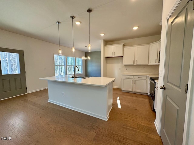 kitchen featuring sink, stainless steel electric range, wood-type flooring, white cabinets, and a center island with sink