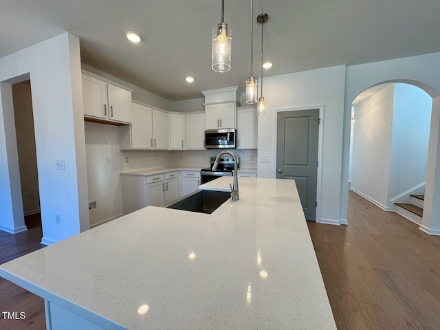 kitchen featuring decorative light fixtures, white cabinetry, an island with sink, stainless steel appliances, and light stone countertops