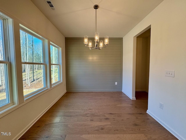 unfurnished dining area featuring wood-type flooring, a notable chandelier, and wood walls