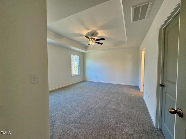 empty room with a raised ceiling, ceiling fan, and carpet flooring