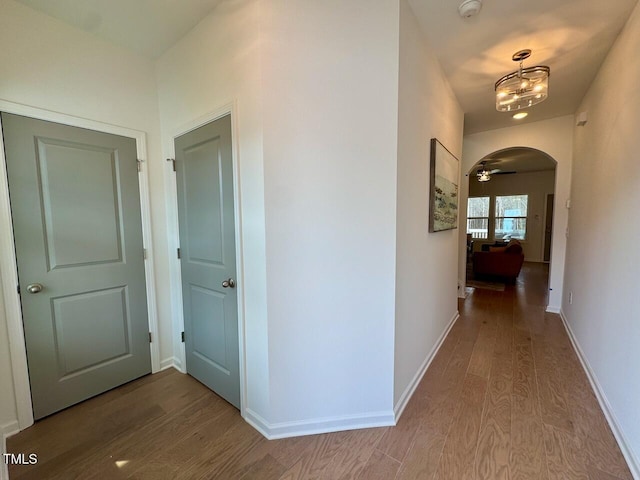 corridor with arched walkways, an inviting chandelier, wood finished floors, and baseboards