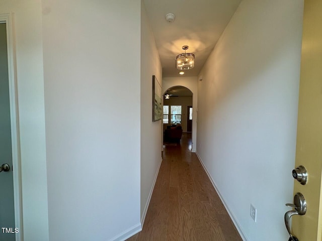 corridor with arched walkways, dark wood-style flooring, and baseboards