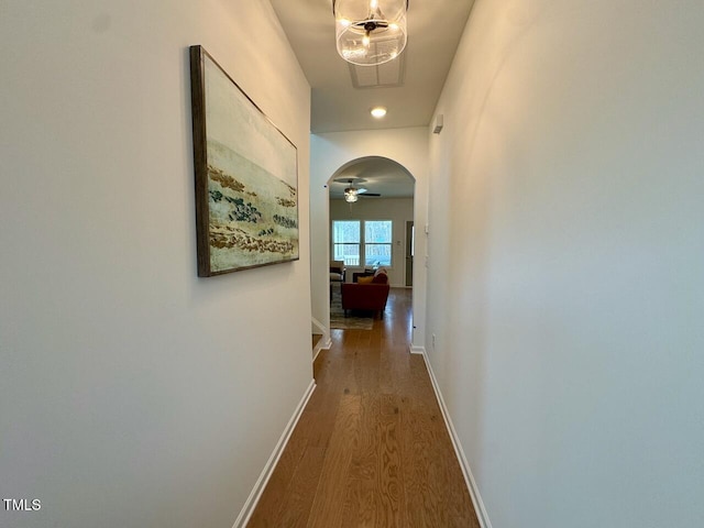 corridor with arched walkways, baseboards, and wood finished floors