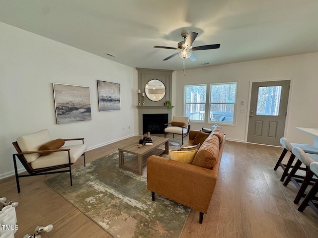 living room with a fireplace, wood finished floors, visible vents, and baseboards