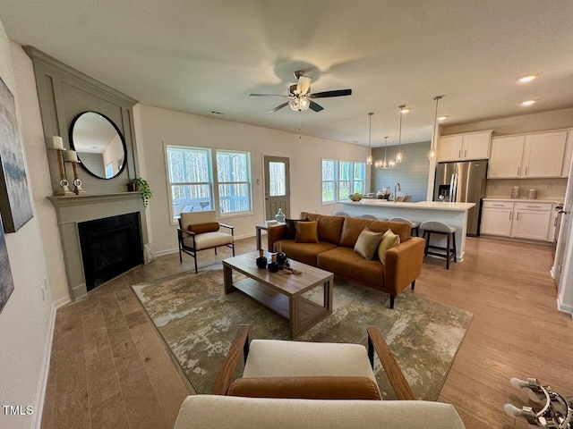 living area featuring light wood-type flooring, a fireplace, baseboards, and ceiling fan