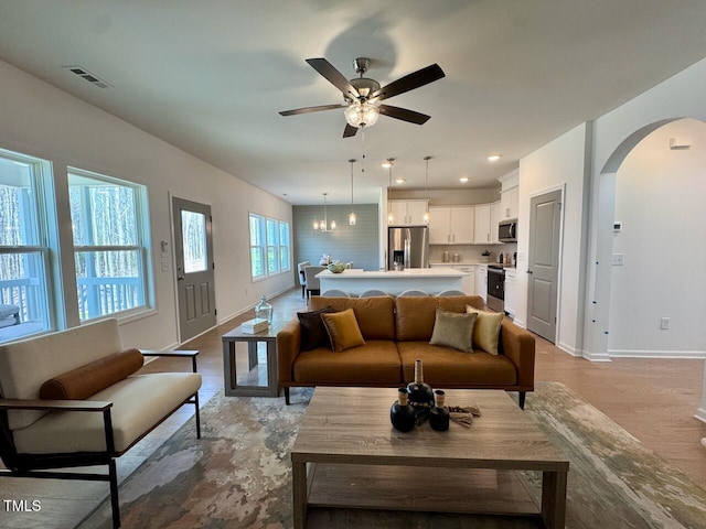 living room with arched walkways, ceiling fan, visible vents, and baseboards