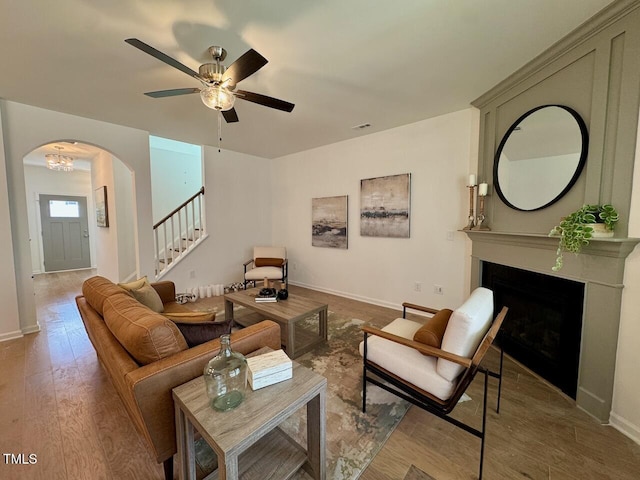 living area featuring arched walkways, a fireplace, stairway, wood finished floors, and baseboards