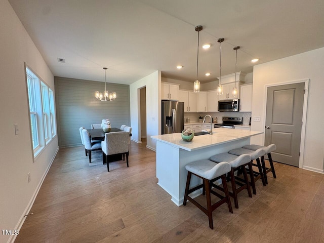 kitchen featuring white cabinets, appliances with stainless steel finishes, light countertops, light wood-type flooring, and a chandelier