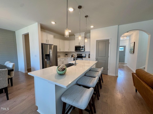 kitchen featuring arched walkways, wood finished floors, light countertops, stainless steel appliances, and a sink