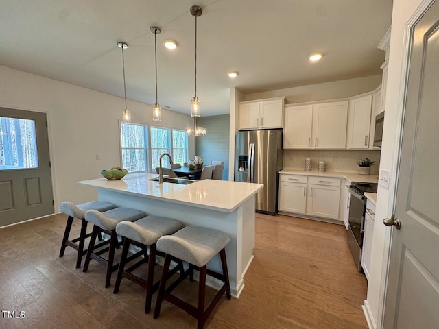 kitchen with a center island with sink, electric range oven, a kitchen bar, stainless steel refrigerator with ice dispenser, and a sink