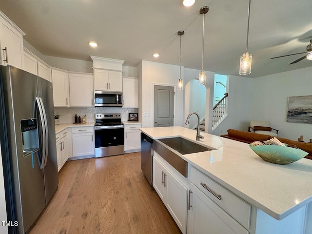 kitchen featuring tasteful backsplash, white cabinets, stainless steel appliances, light wood-style floors, and a sink