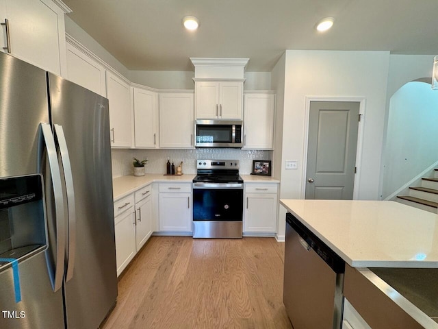 kitchen featuring stainless steel appliances, light countertops, decorative backsplash, and light wood finished floors