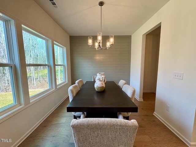 dining space featuring a chandelier, wooden walls, wood finished floors, visible vents, and baseboards