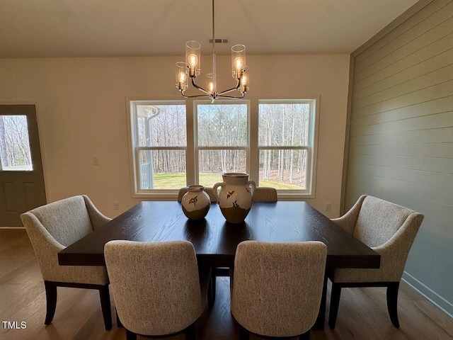 dining area with an inviting chandelier, visible vents, wood finished floors, and wood walls