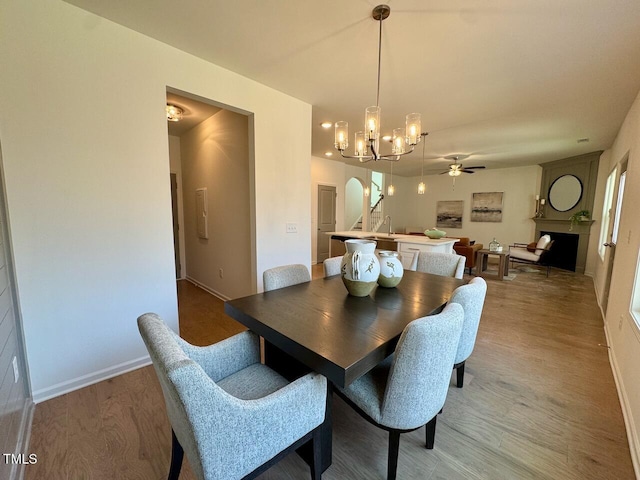 dining space with ceiling fan, arched walkways, a large fireplace, wood finished floors, and baseboards