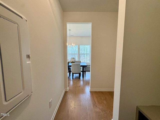 corridor with baseboards, an inviting chandelier, and wood finished floors