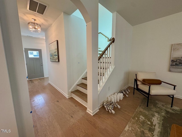 foyer entrance with arched walkways, stairs, wood finished floors, and visible vents