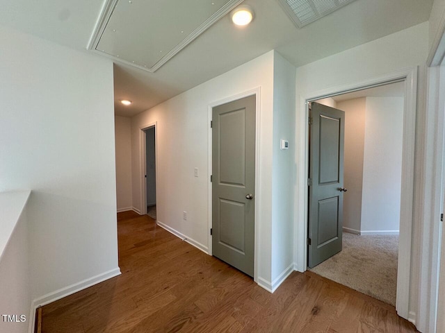 hallway featuring attic access, visible vents, baseboards, and wood finished floors