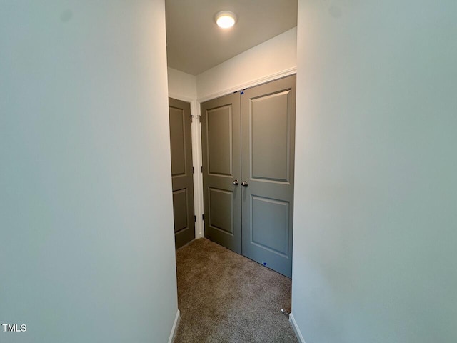 corridor featuring baseboards and dark colored carpet