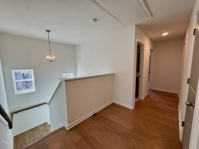 corridor featuring attic access, baseboards, wood finished floors, an upstairs landing, and a chandelier