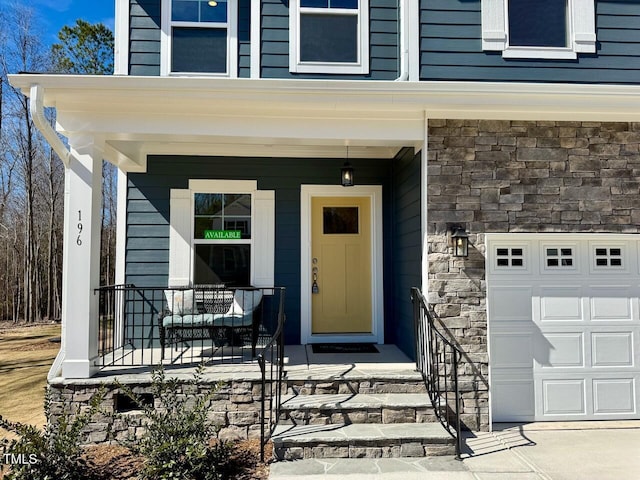 view of exterior entry with a garage, stone siding, and a porch