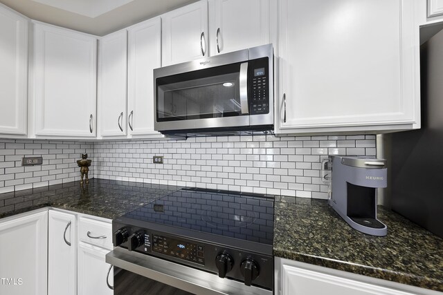 kitchen with range, white cabinets, backsplash, and dark stone countertops