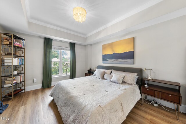 bedroom featuring light hardwood / wood-style floors, crown molding, and a tray ceiling