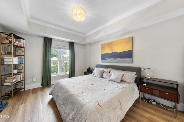 bedroom featuring wood-type flooring, ornamental molding, and a raised ceiling