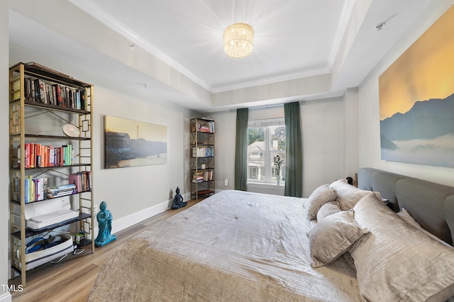 bedroom with crown molding, wood-type flooring, a raised ceiling, and an inviting chandelier