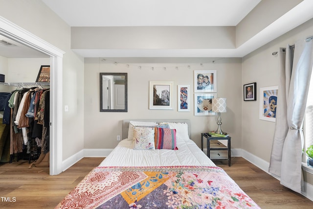 bedroom with a walk in closet, wood-type flooring, and a closet