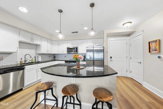 kitchen featuring appliances with stainless steel finishes, white cabinets, sink, light wood-type flooring, and a center island