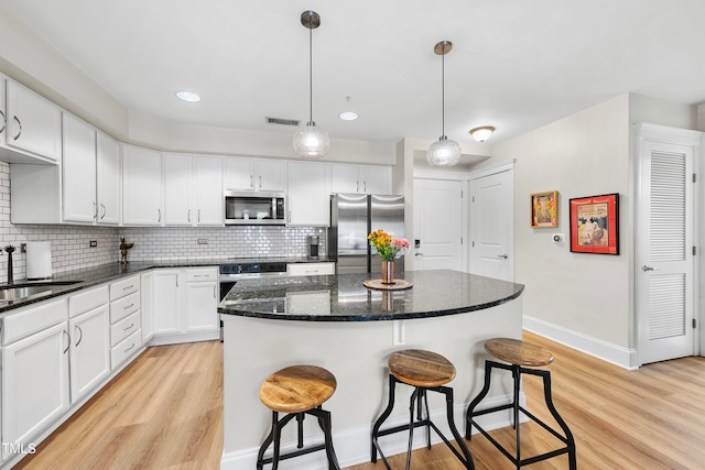 kitchen with appliances with stainless steel finishes, white cabinetry, a center island, and light wood-type flooring