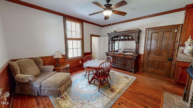 living area featuring ceiling fan, ornamental molding, wood finished floors, and wainscoting