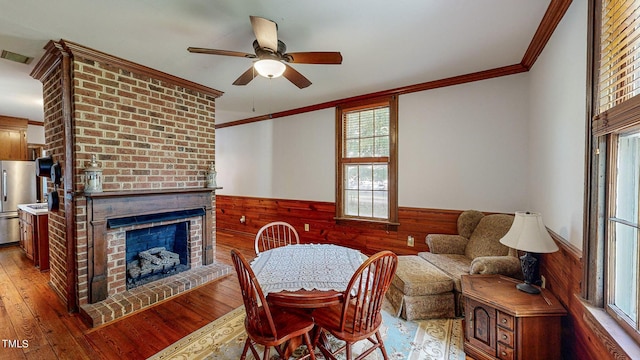 dining area with wooden walls, a fireplace, wood finished floors, wainscoting, and crown molding