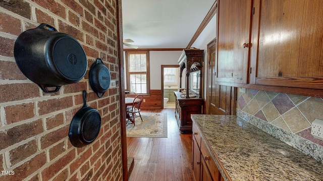 interior space featuring light stone counters, wood finished floors, wainscoting, brown cabinets, and crown molding