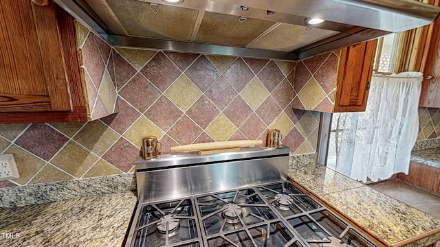 kitchen featuring tile countertops, tasteful backsplash, brown cabinetry, stainless steel gas stove, and wall chimney exhaust hood