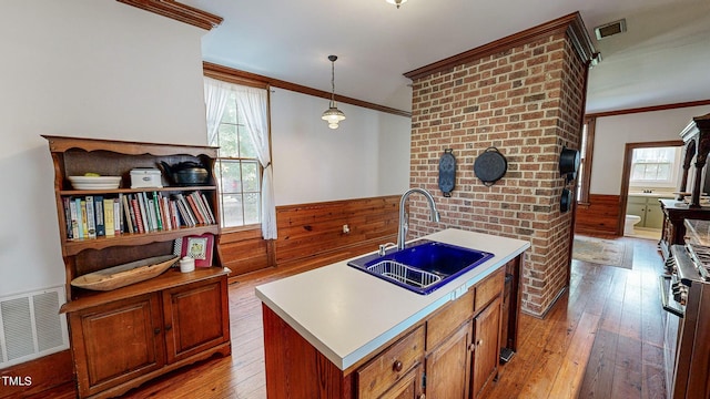 kitchen featuring light countertops, wainscoting, a sink, and a center island with sink